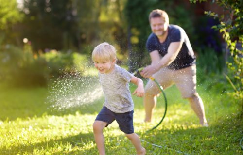 Father having backyard fun with son, using hose.
