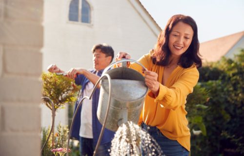 Husband and wife gardening together in new spacious backyard at Arista McKinney, wife is featured in yellow shirt pouring water out of pail.